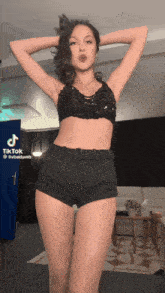 a woman in a black top and shorts is standing in front of a sign that says tiktok