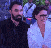a man with a beard and glasses is standing next to a woman in a white coat .