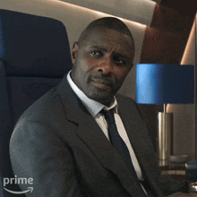 a man in a suit and tie is sitting in a chair with an amazon prime logo on the bottom right
