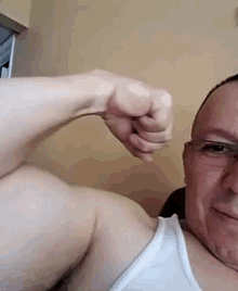 a man with glasses is flexing his muscles in a white tank top .