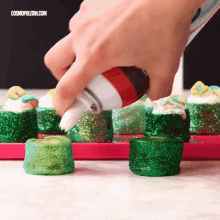 a person is pouring frosting on a tray of green candy .