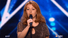 a woman singing into a microphone with a nbc logo in the corner