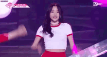 a woman is standing on a stage wearing a white crop top and red skirt .