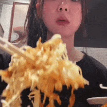 a woman is eating noodles with chopsticks while looking at the camera