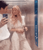 a man taking a picture of a woman in an elevator with his phone