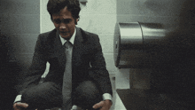 a man is kneeling down in a bathroom next to a toilet paper dispenser