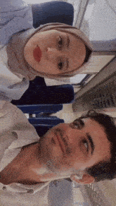 a man and a woman are sitting next to each other on a train and the woman is wearing a hijab