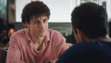 a man in a pink striped shirt sits at a table with another man in a blue shirt