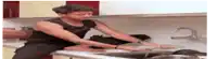 a man in a black tank top is sitting at a kitchen counter washing dishes .