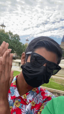 a man wearing a face mask and sunglasses stands in front of a fountain