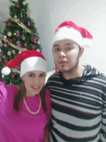 a man and a woman wearing santa hats pose for a photo in front of a christmas tree