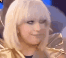 a woman with blonde hair and a gold jacket is smiling