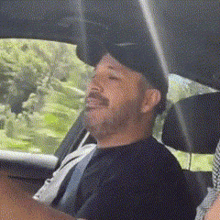 a man in a baseball cap is sitting in the driver 's seat of a car with his eyes closed .