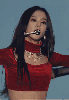 a woman is wearing a red crop top and a necklace while singing into a microphone .