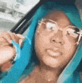 a woman with blue hair and glasses is sitting in a car and taking a selfie .