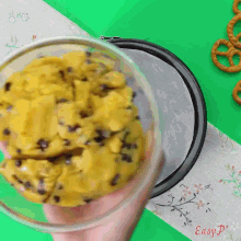 a bowl of cookie dough is being poured into a pan with pretzels in the background