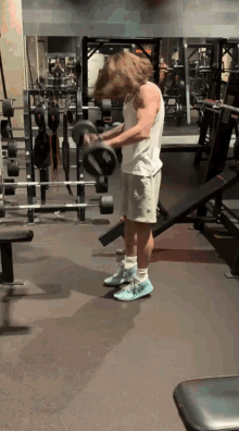 a man in a white tank top is lifting dumbbells in a gym