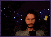 a man with long hair and a beard is sitting in front of a microphone .