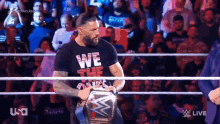 roman reigns is standing in a wrestling ring holding a championship belt .