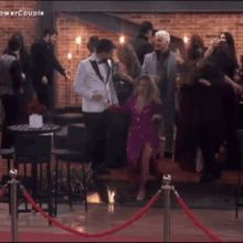 a woman in a purple dress is dancing on a red carpet in front of a crowd with the words power couple on the wall