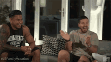 two men are sitting on a couch and laughing .