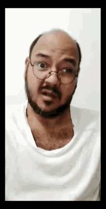 a bald man with a beard and glasses is wearing a white shirt and making a funny face .
