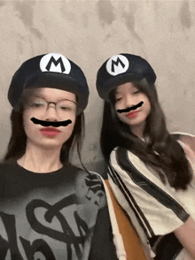 two girls wearing hats with the letter m on them and fake mustaches on their faces .