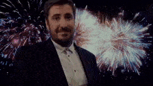 a man in a suit and white shirt is standing in front of a fireworks display .