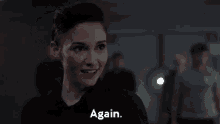 a woman in a black shirt is standing in front of a group of people and saying `` again '' .