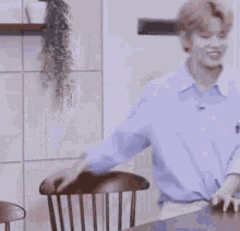 a man in a blue shirt is standing next to a wooden chair and a table .