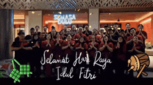 a group of people standing in front of a sign that says selamat hari raya idul fitri