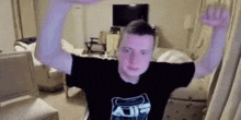 a man in a black shirt is standing in a living room with his arms in the air .