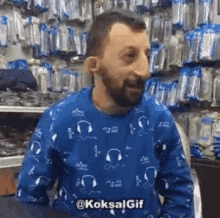 a man with a beard wearing a blue sweater is sitting in front of a shelf .