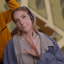 a woman wearing headphones and a blue jacket waves