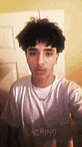 a young man with curly hair is wearing a white shirt with the word lachino on it .