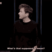 a man in a black shirt is standing in front of a curtain and talking to someone .