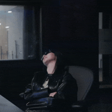 a woman wearing sunglasses sits in a dark room