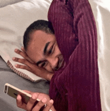 a man is laying on a bed with a blanket over his head and looking at his phone