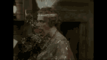 a woman in a dress and headband is holding a bouquet of flowers in her hand .