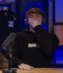 a man wearing headphones and a supreme hoodie laughs