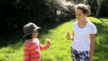 two girls are standing in the grass one is holding an ice cream cone and the other is wearing a hat