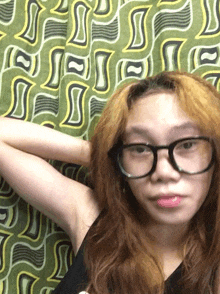 a woman wearing glasses is standing in front of a green and yellow patterned background