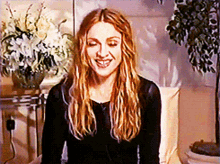 a woman with long blonde hair is smiling in front of flowers