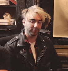a man with blonde hair is wearing a black leather jacket and a white shirt