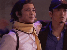 a man wearing a hat with the letter s on it stands next to a man wearing a scarf