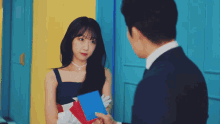 a woman in a blue dress stands next to a man in a suit holding envelopes