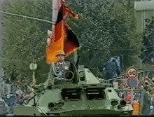a soldier stands on top of a military vehicle with a flag flying in the background and a sign that says 60