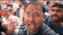 a man wearing glasses is screaming in a crowd of people .