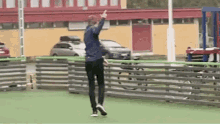 a man is jumping over a fence on a soccer field while giving the middle finger .