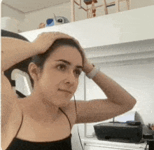 a woman in a black tank top holds her head